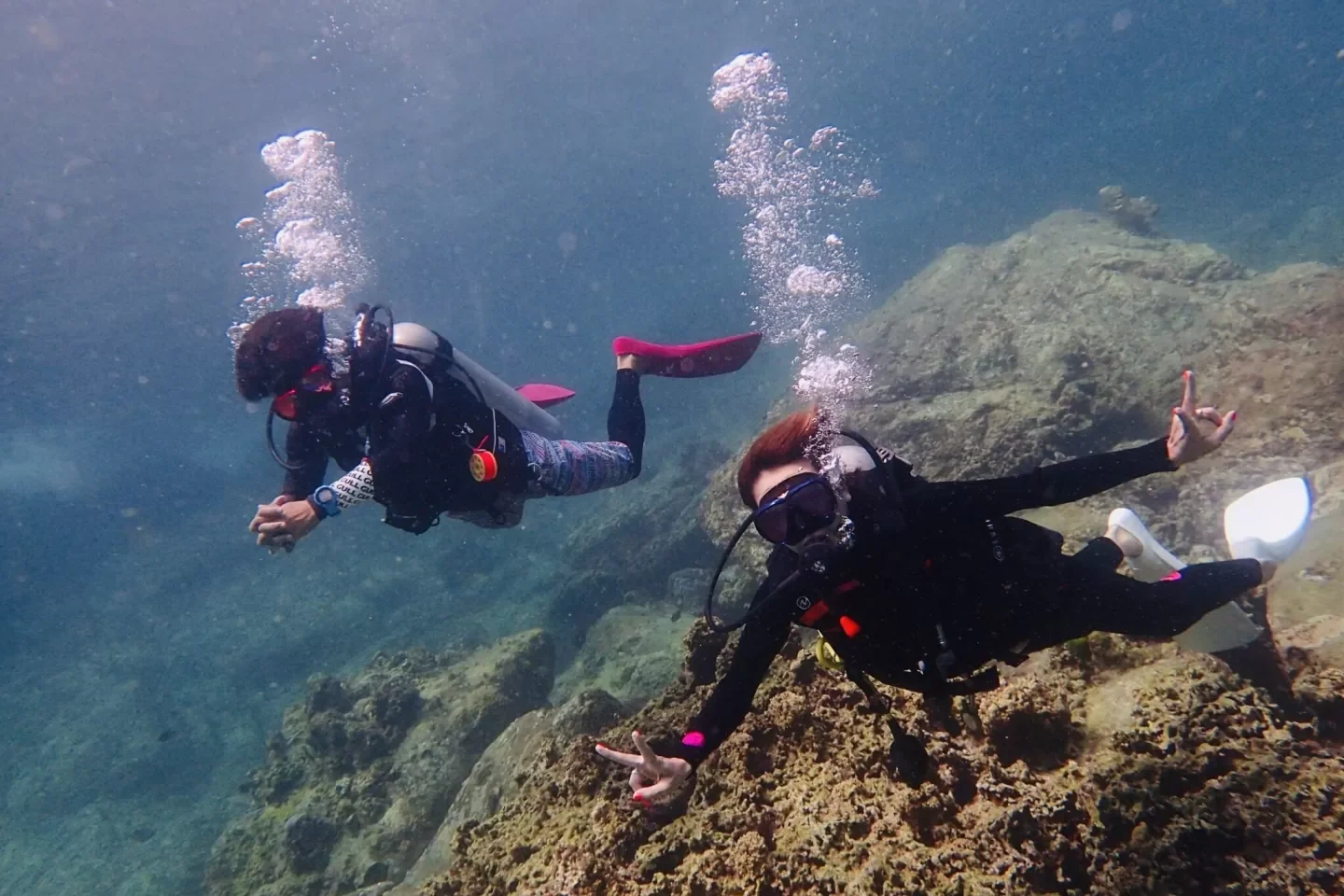 Two divers enjoying fun diving over a rocky reef in Phuket